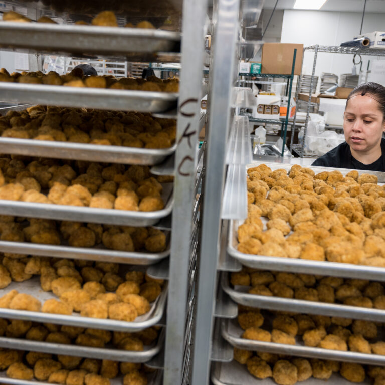 Food service team member behind racks of food on sheet pans