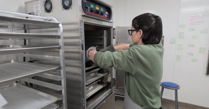Food service worker placing pans of food in cook & hold oven