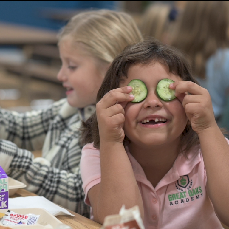 Elementary student holding cucumber slices over her eyes